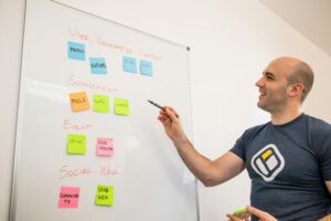 Smiling man presents strategies on a whiteboard with post-its, focusing on engagement and user-generated content.